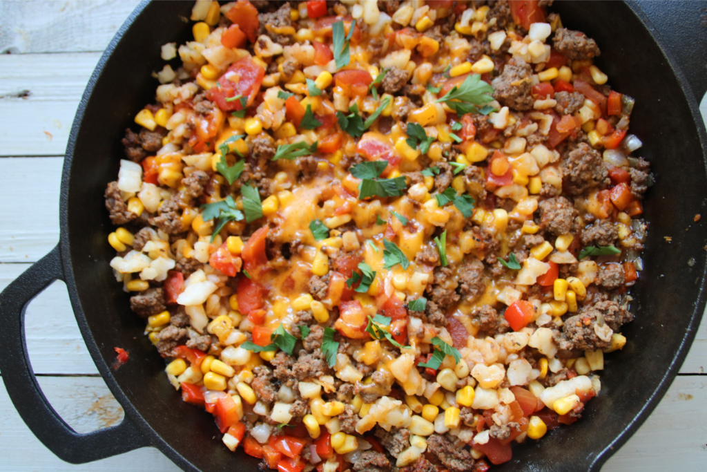Lost Treasure Skillet made with ground beef, hash browns, diced tomatoes, corn, and melted cheddar cheese in a cast iron pan