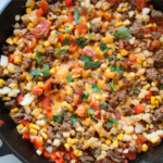 Lost Treasure Skillet made with ground beef, hash browns, diced tomatoes, corn, and melted cheddar cheese in a cast iron pan