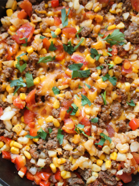 Lost Treasure Skillet made with ground beef, hash browns, diced tomatoes, corn, and melted cheddar cheese in a cast iron pan
