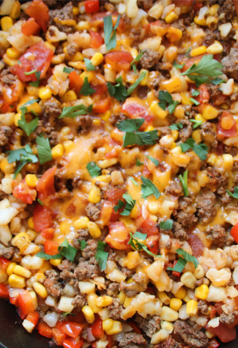 Lost Treasure Skillet made with ground beef, hash browns, diced tomatoes, corn, and melted cheddar cheese in a cast iron pan