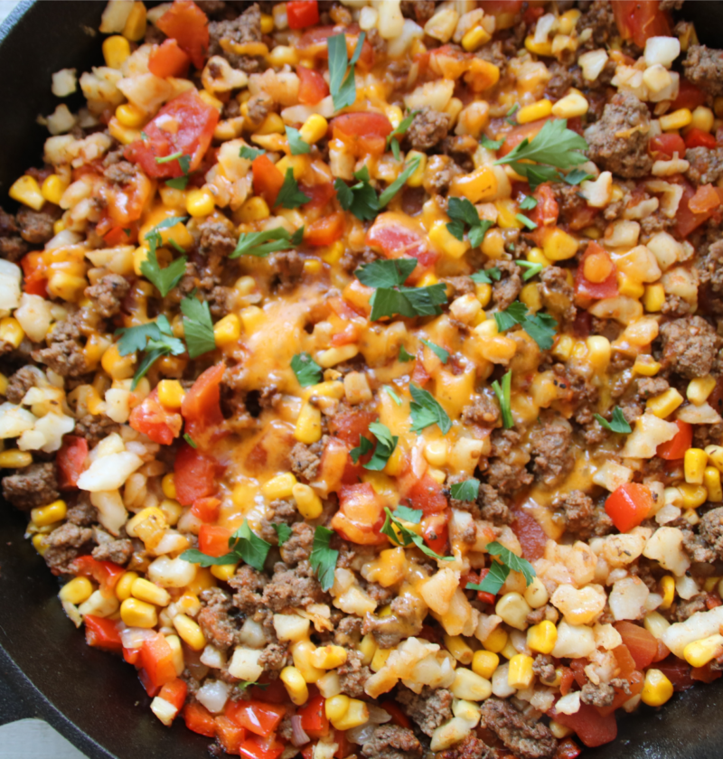 Lost Treasure Skillet made with ground beef, hash browns, diced tomatoes, corn, and melted cheddar cheese in a cast iron pan