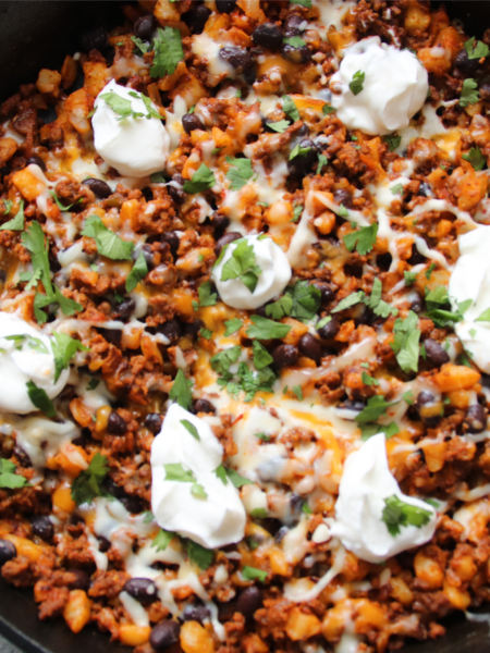 Lonely Campfire Taco Hash Skillet with ground beef, hash browns, melted Tex-Mex cheese, and sour cream in a cast iron skillet