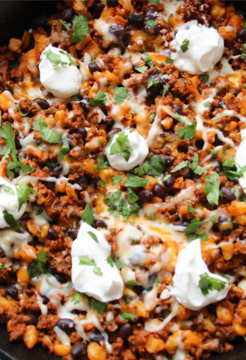 Lonely Campfire Taco Hash Skillet with ground beef, hash browns, melted Tex-Mex cheese, and sour cream in a cast iron skillet