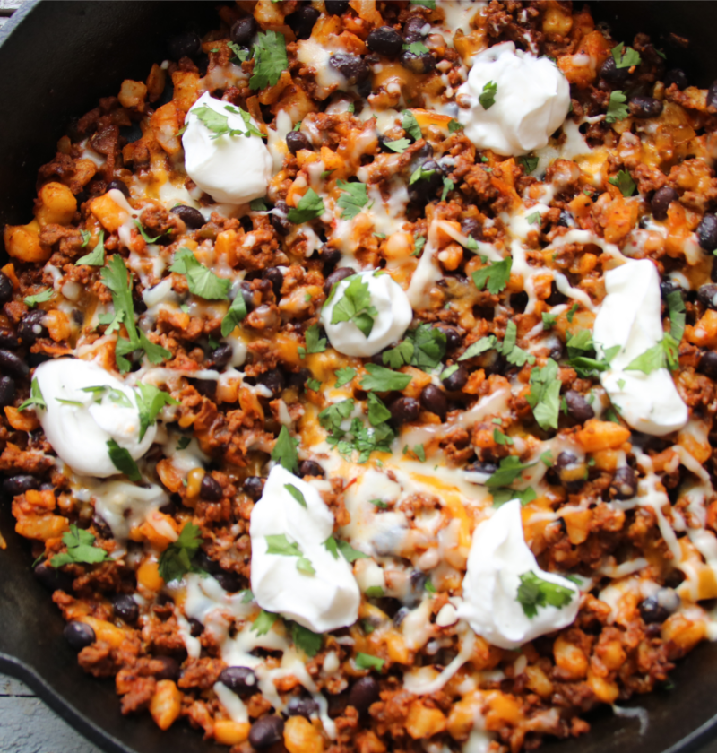 Lonely Campfire Taco Hash Skillet with ground beef, hash browns, melted Tex-Mex cheese, and sour cream in a cast iron skillet