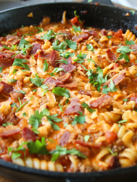 Grandpa's One Pan Ground Beef & Bacon Supper served in a cast iron skillet with rotini pasta, crispy bacon, melted cheddar cheese, and parsley garnish.