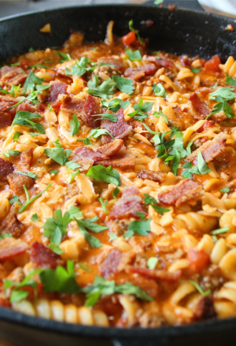Grandpa's One Pan Ground Beef & Bacon Supper served in a cast iron skillet with rotini pasta, crispy bacon, melted cheddar cheese, and parsley garnish.