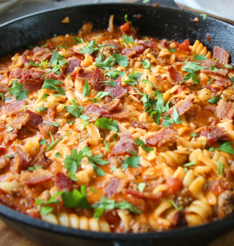 Grandpa's One Pan Ground Beef & Bacon Supper served in a cast iron skillet with rotini pasta, crispy bacon, melted cheddar cheese, and parsley garnish.