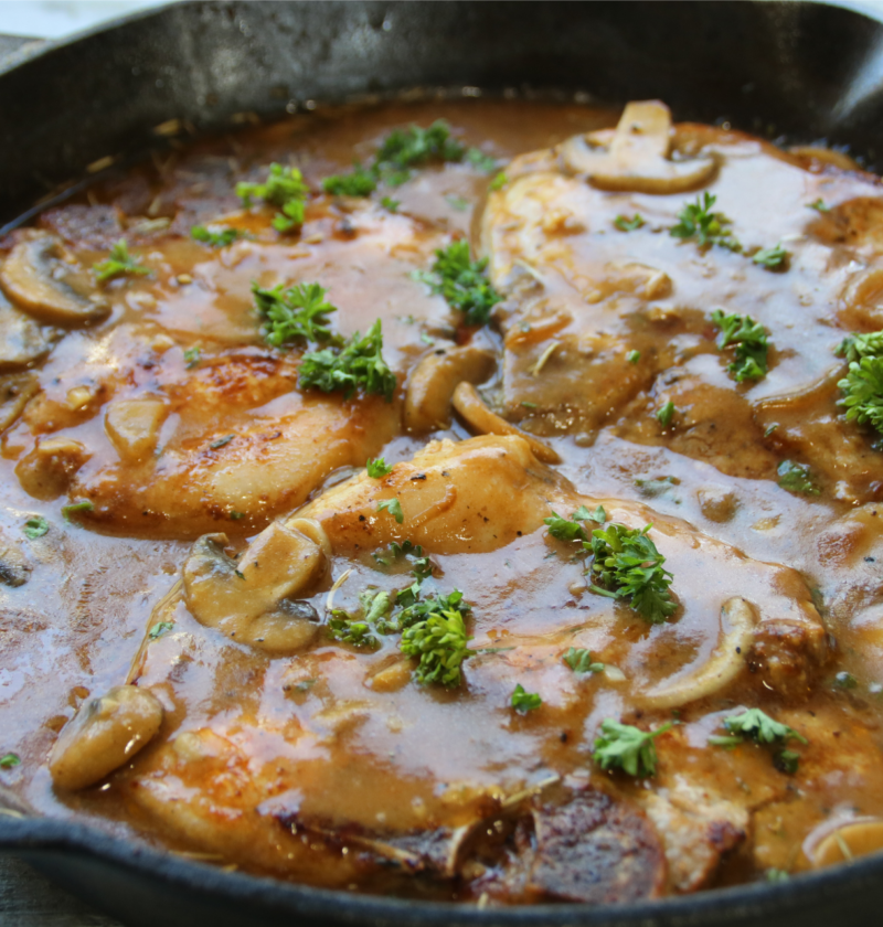Smothered pork chops covered in rich onion mushroom gravy served with mashed potatoes and green beans in a hearty old-fashioned comfort supper.
